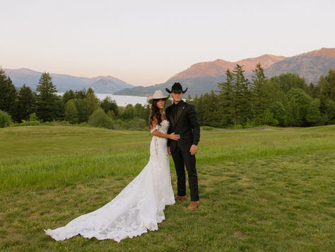A bride and groom posed side by side in a field at Skamania Lodge with hills and evergreen trees in the background as the sun is setting.