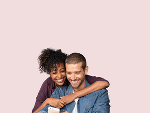 Smiling couple looking at a phone together, reading an online memorial page that honors a loved one’s life.