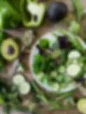 A fresh green salad sits on a wooden table surrounded by whole ingredients including avocado, cucumber, green beans, broccoli, herbs, and sprouts. The vibrant, nourishing produce reflects Holsm’s approach to hormone-friendly nutrition—supportive, satisfying, and grounded in whole foods that fuel sustainable strength and energy.