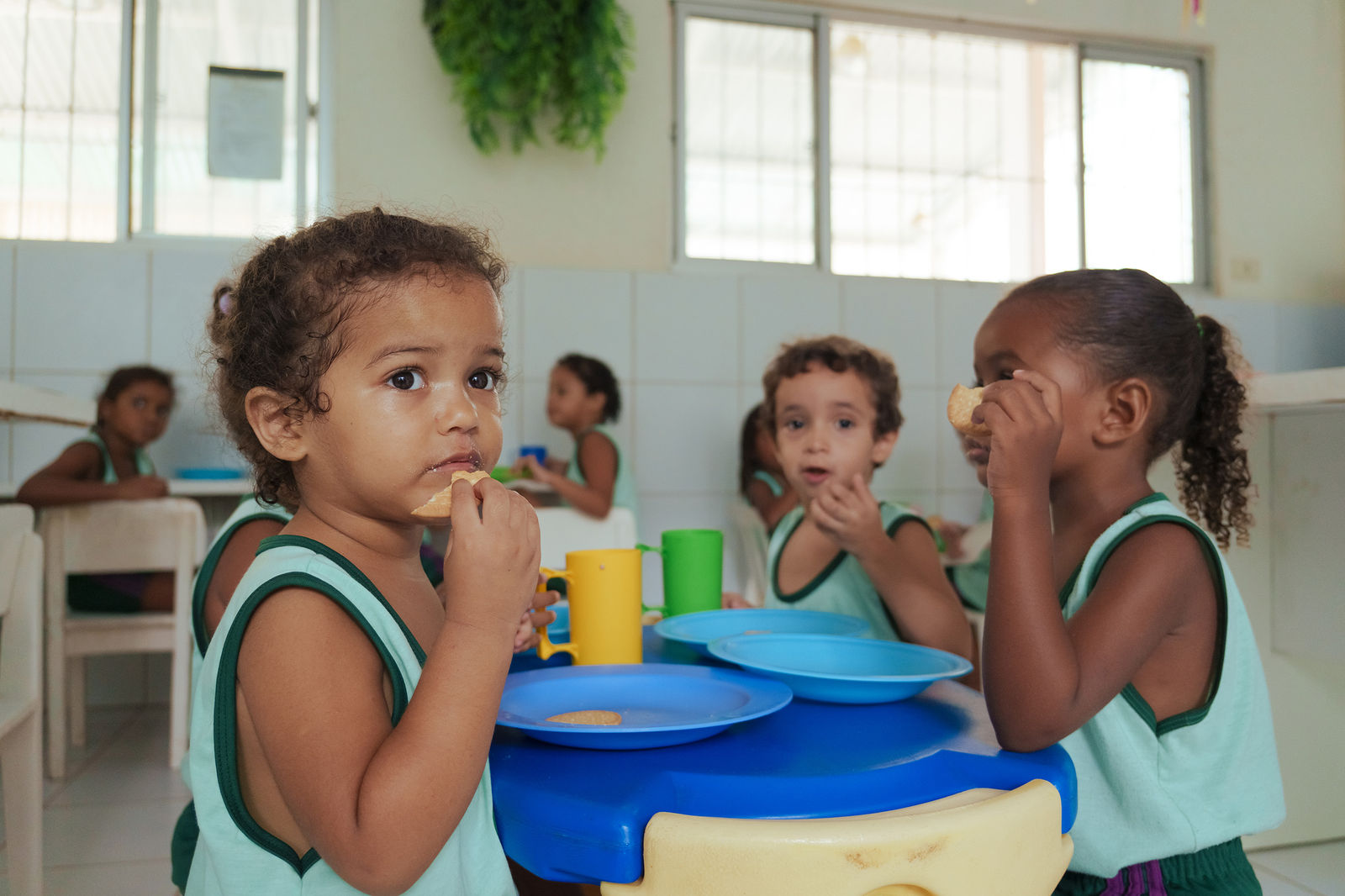 Crianças fazendo o lanche em volta de uma mesa azul