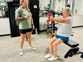 Trainer watching her elderly client sit on a bench and workout with dumbbells