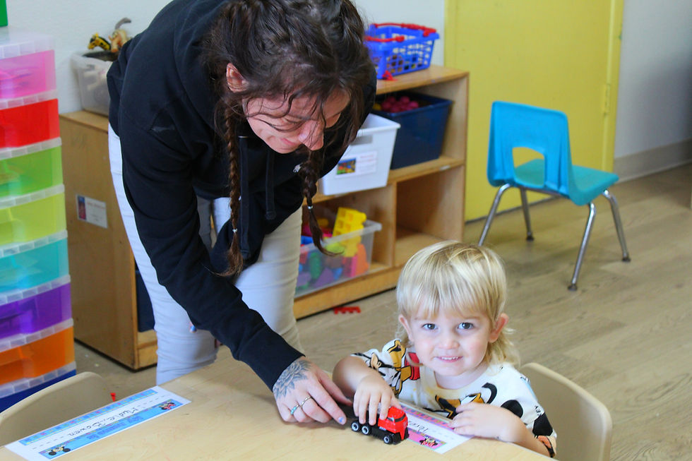 A teacher and toddler in the classroom at the table playing with a toy truck at WCA