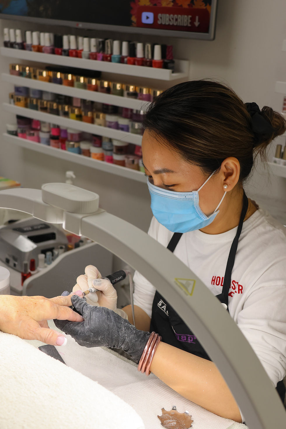 A naile technician holding her client's hand under the lamp as she files down her nails.