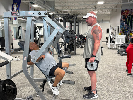 A man doing chest press with his trainer standing in front of him holding more weight