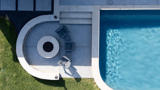 Above view of a fire pit with lawn chairs in a semi circle to the left a pool