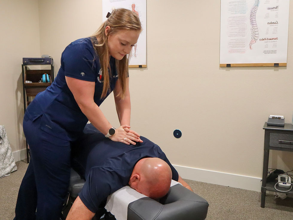 A female chiropractor is adjusting the back of male client on an adjustment table.