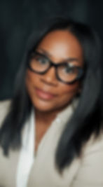 Barbara Walker in a light blazer and glasses, smiling confidently with a dark studio backdrop.