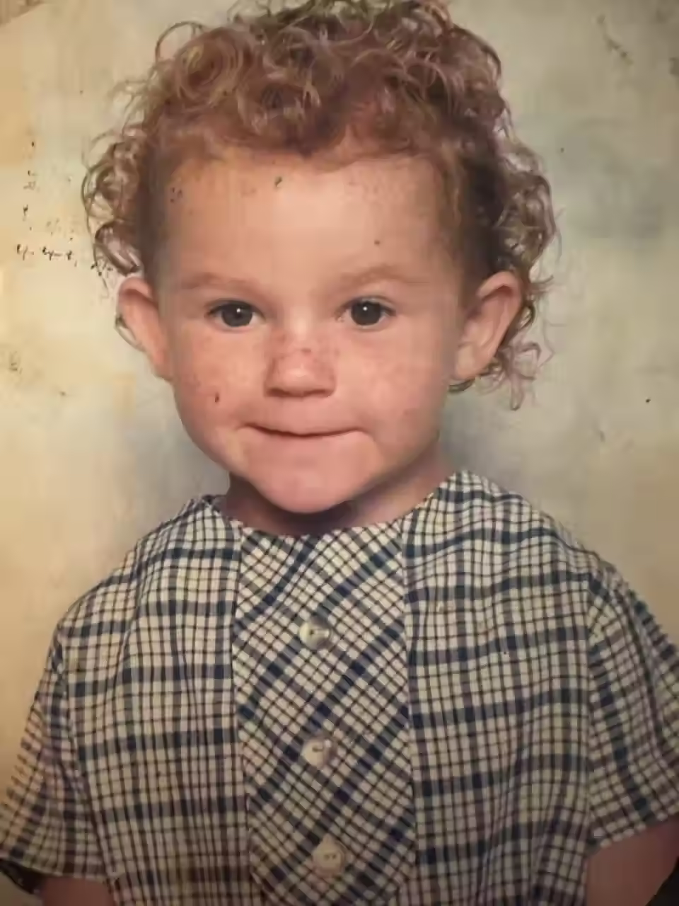 Jessica Gaudie smiling as a child in a plaid dress.