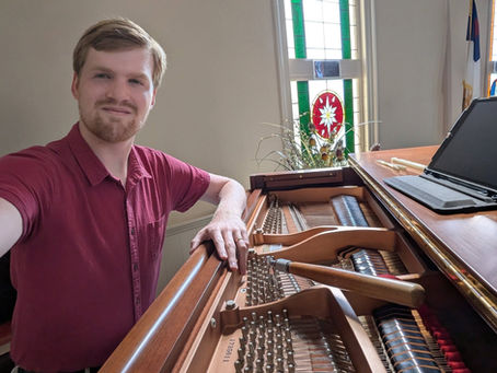 Ryan Hacker smiling while tuning a grand piano