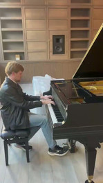 A man playing a black Knabe grand piano