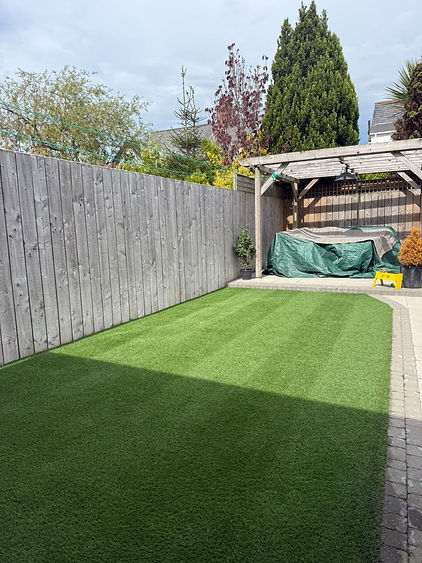 Well-maintained artificial grass lawn in a backyard garden next to a wooden fence and a sheltered seating area.
