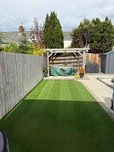Clean artificial grass lawn in a residential backyard beside a tall wooden fence and patio area.