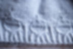 Close-up of a light blue knitted sweater with cable-knit pattern and ribbed hem, showing soft textured fabric. Pattern By Wool & Wyrd.