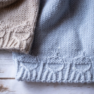 A detailed view of two folded, hand-knit wool beanies stacked on top of each other, highlighting the rich, textured cable stitches in the fabric. Pattern by Wool & Wyrd.