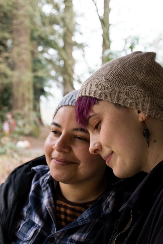 A happy couple put their heads together in peace. They are wearing Acorn Street Beanies and the stitches along the brim form sweet little acorns.