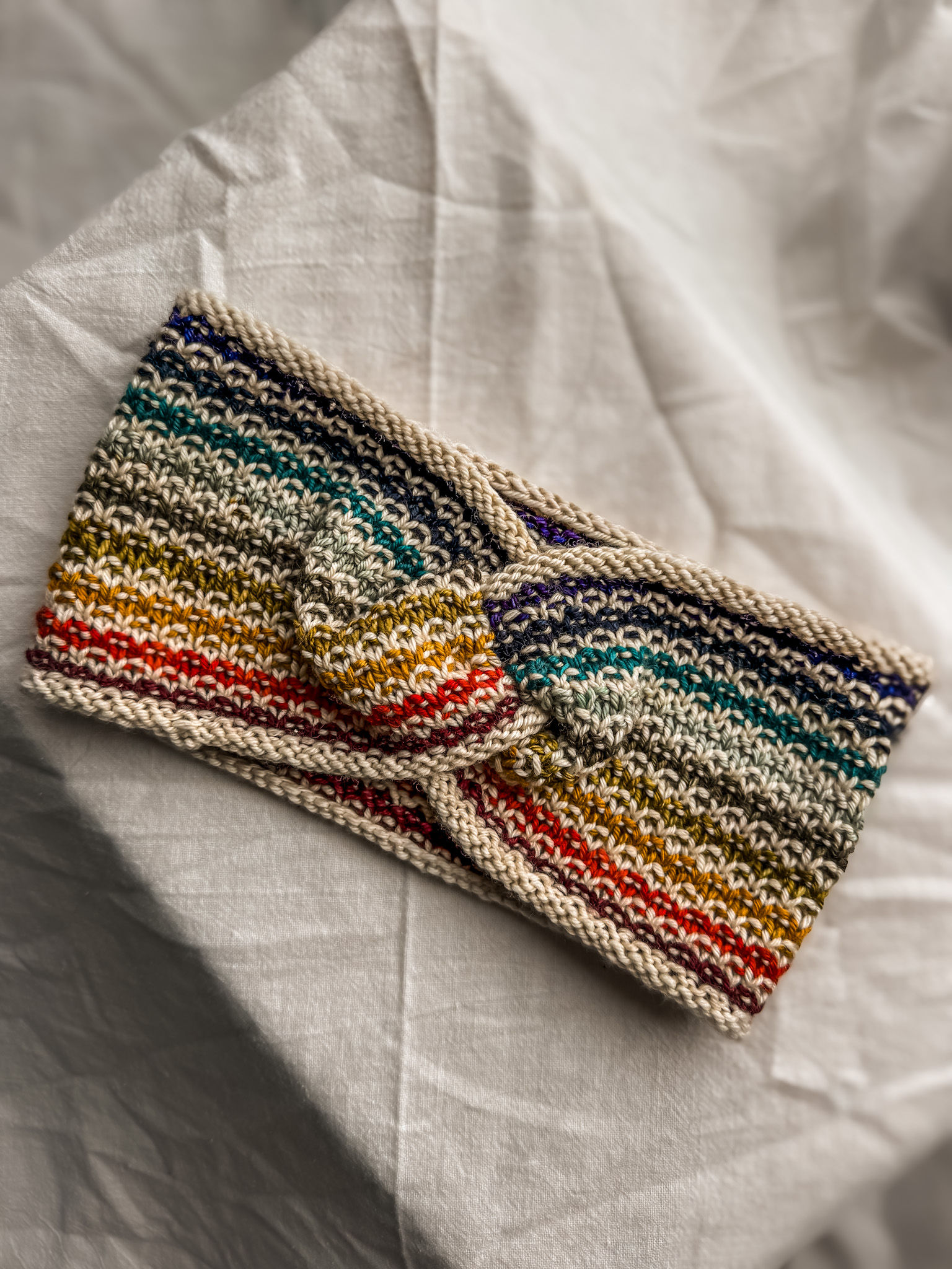 Easy headband knitting pattern in colorful striped yarn, shown flat with a simple twist detail.