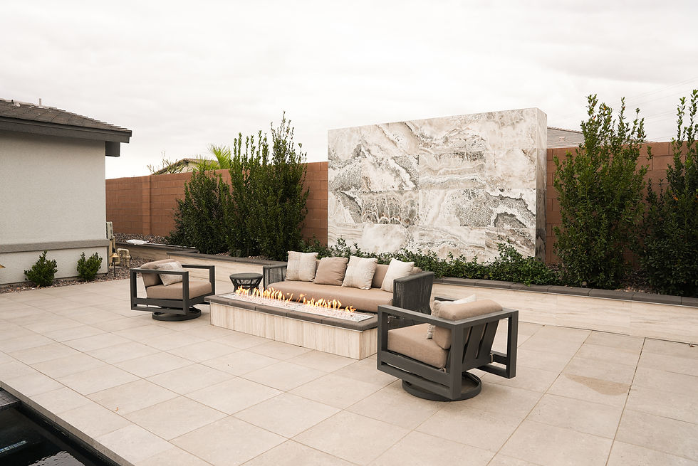 Modern outdoor seating area featuring a sleek fire pit, surrounded by contemporary chairs and a sofa, set against a textured stone wall and lush greenery.