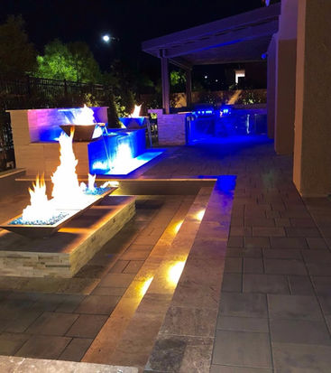 Luxurious backyard at night with fire pit, water features, and landscape lighting