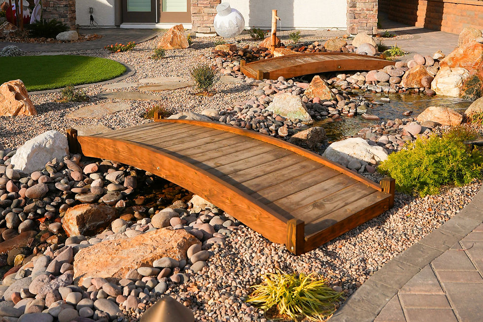 A tranquil garden scene featuring two small wooden bridges crossing over a decorative stream, surrounded by stones and lush greenery.