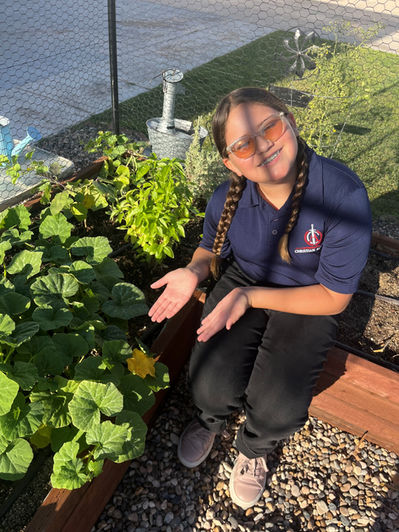 A brunette female student in braids displays the pumpkin plants she has been growing in her horticulture class