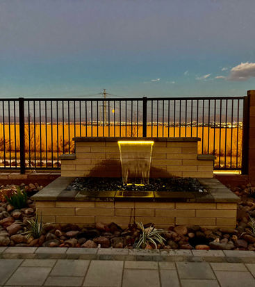 Modern backyard water feature illuminated at dusk with stone accents