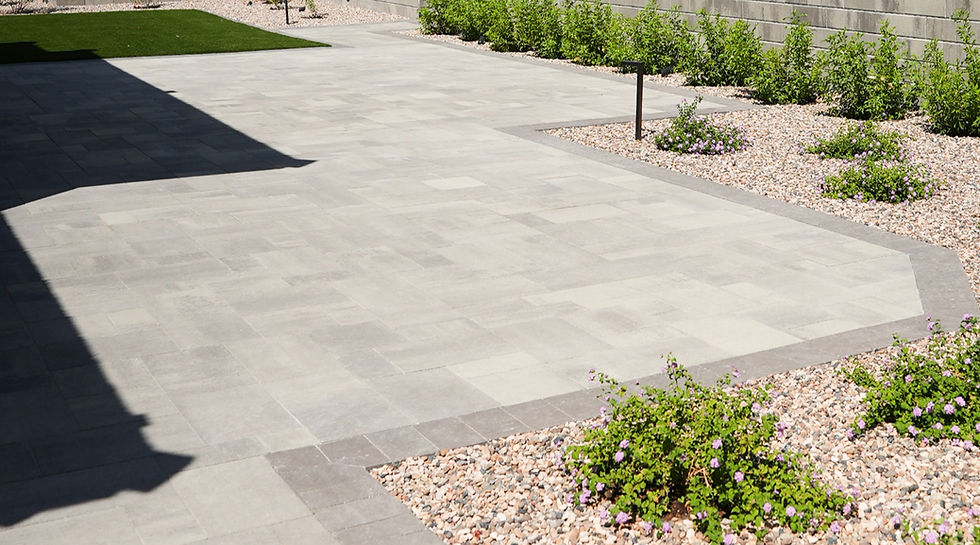 Modern patio design featuring sleek concrete landscaping pavers, bordered by lush greenery and decorative pebble accents.