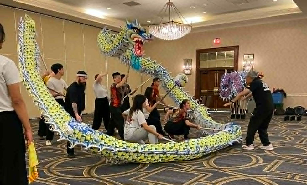 People practice a dragon dance indoors, lifting a colorful dragon puppet. The room has patterned carpet and chandeliers, creating a lively scene.