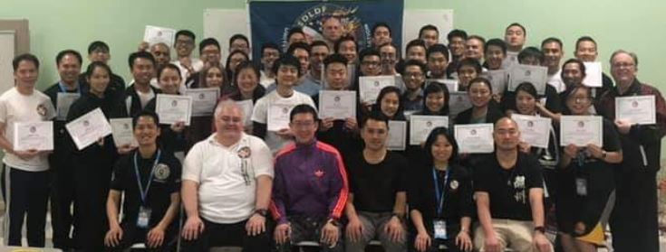 Group of people posing with certificates, smiling in a room. A banner in the background. Casual attire, diverse group, celebratory mood.