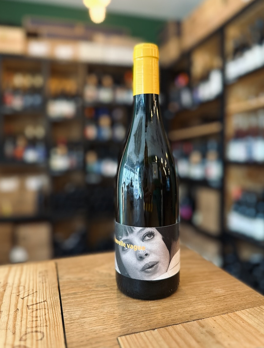 bouteille de vin blanc Nouvelle vague du domaine Nouvelle Donne en Roussillon présentée debout devant une étagère remplie de bouteilles