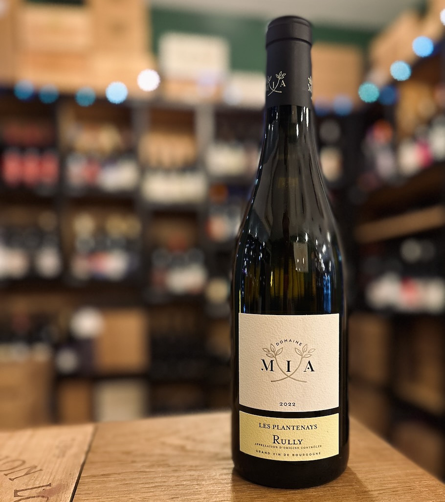 bouteille de vin blanc du domaine Mia en Bourgogne présentée debout devant une étagère remplie de bouteilles