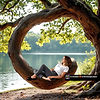 Une branche d’arbre arrondie sert d’appui et de balançoire naturelle à une femme qui s’allonge dessus au bord de l’eau. Souti