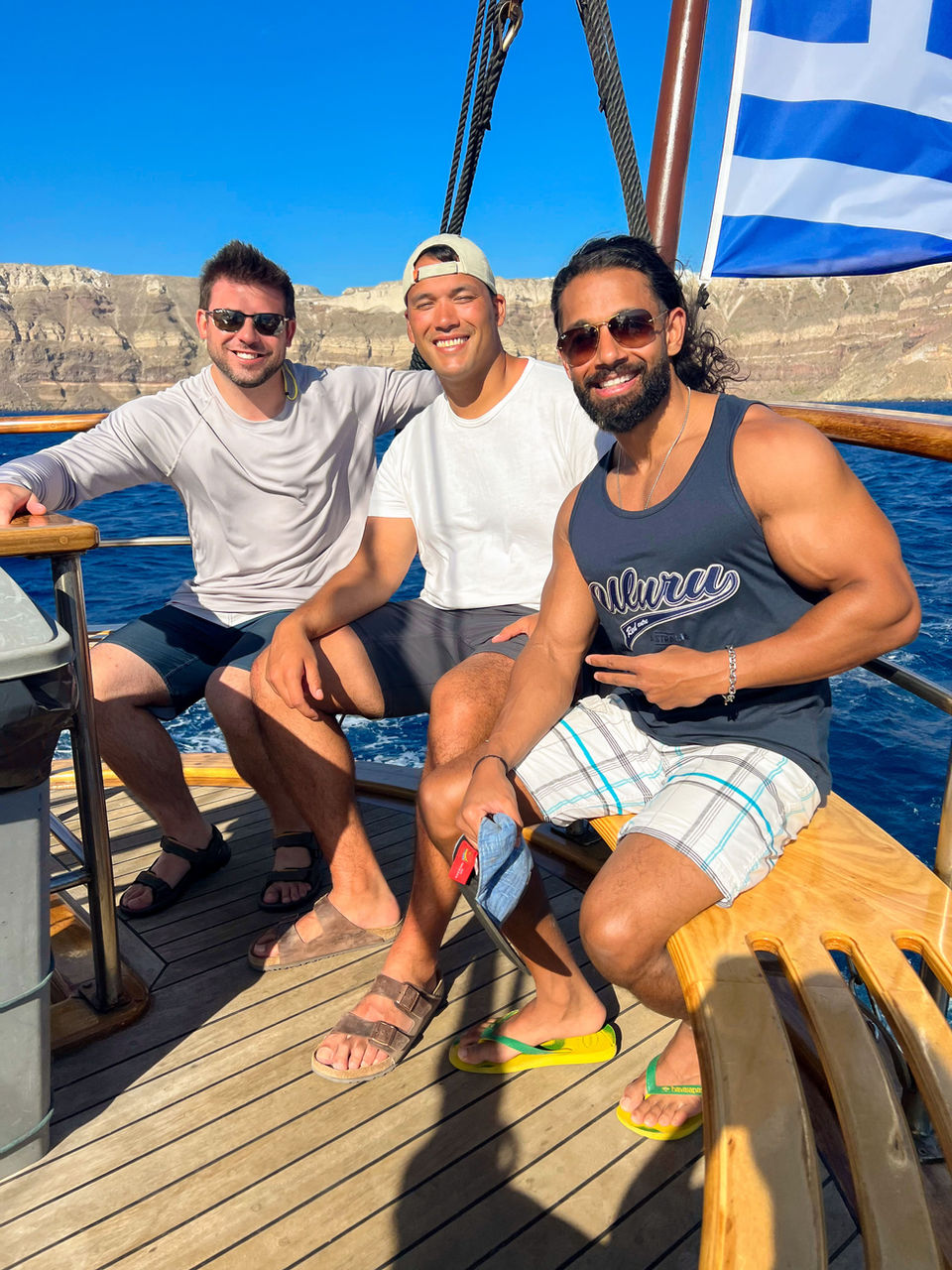 Three friends smiling on a boat trip in Santorini with cliffs in the background.
