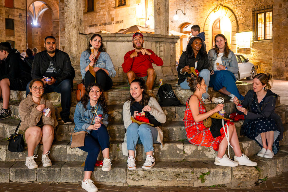 Group of FTLO friends sitting on stone steps at night in a Tuscan hill town