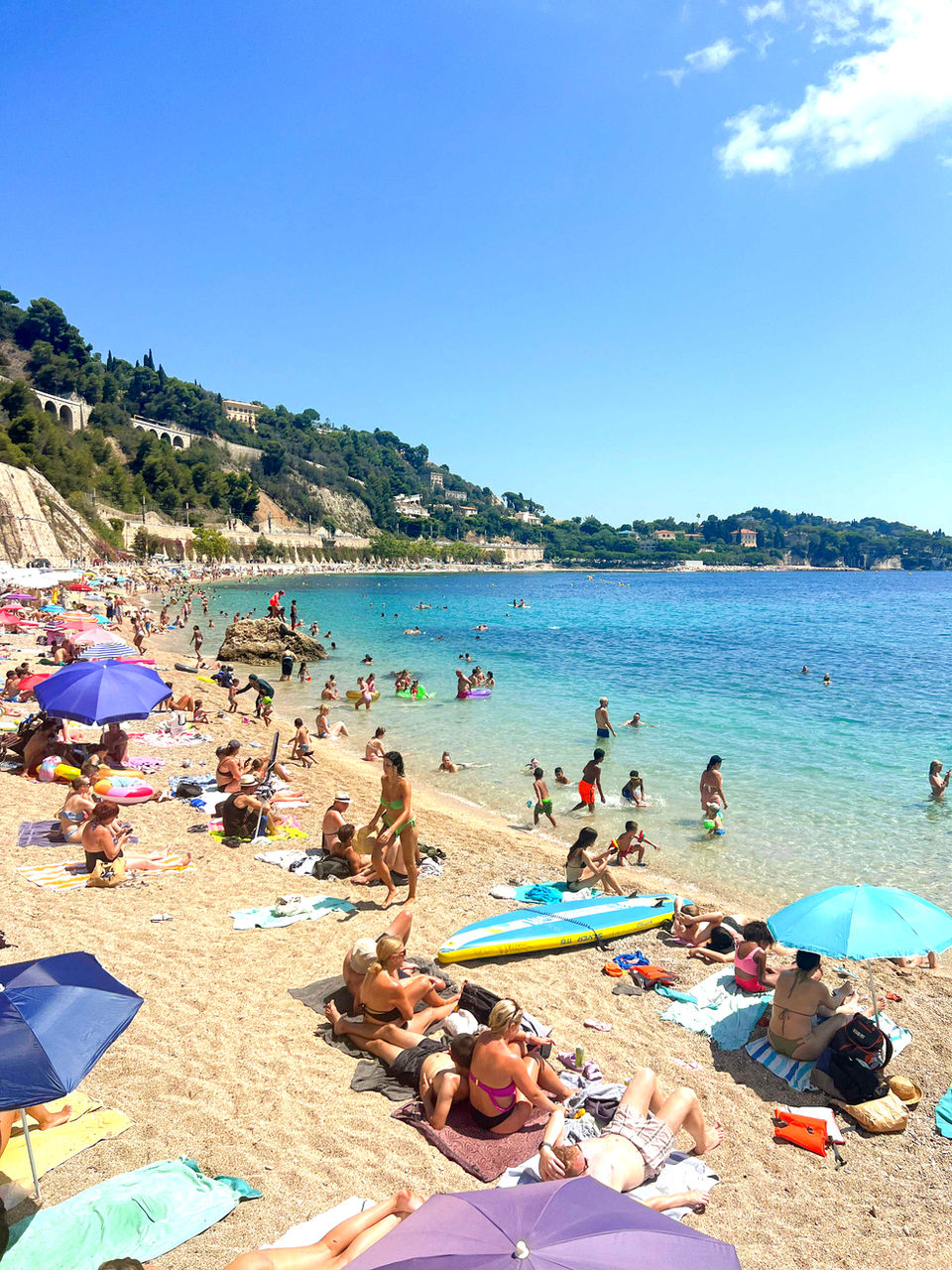 Crowded beach day with colorful umbrellas and swimmers on the French Riviera
