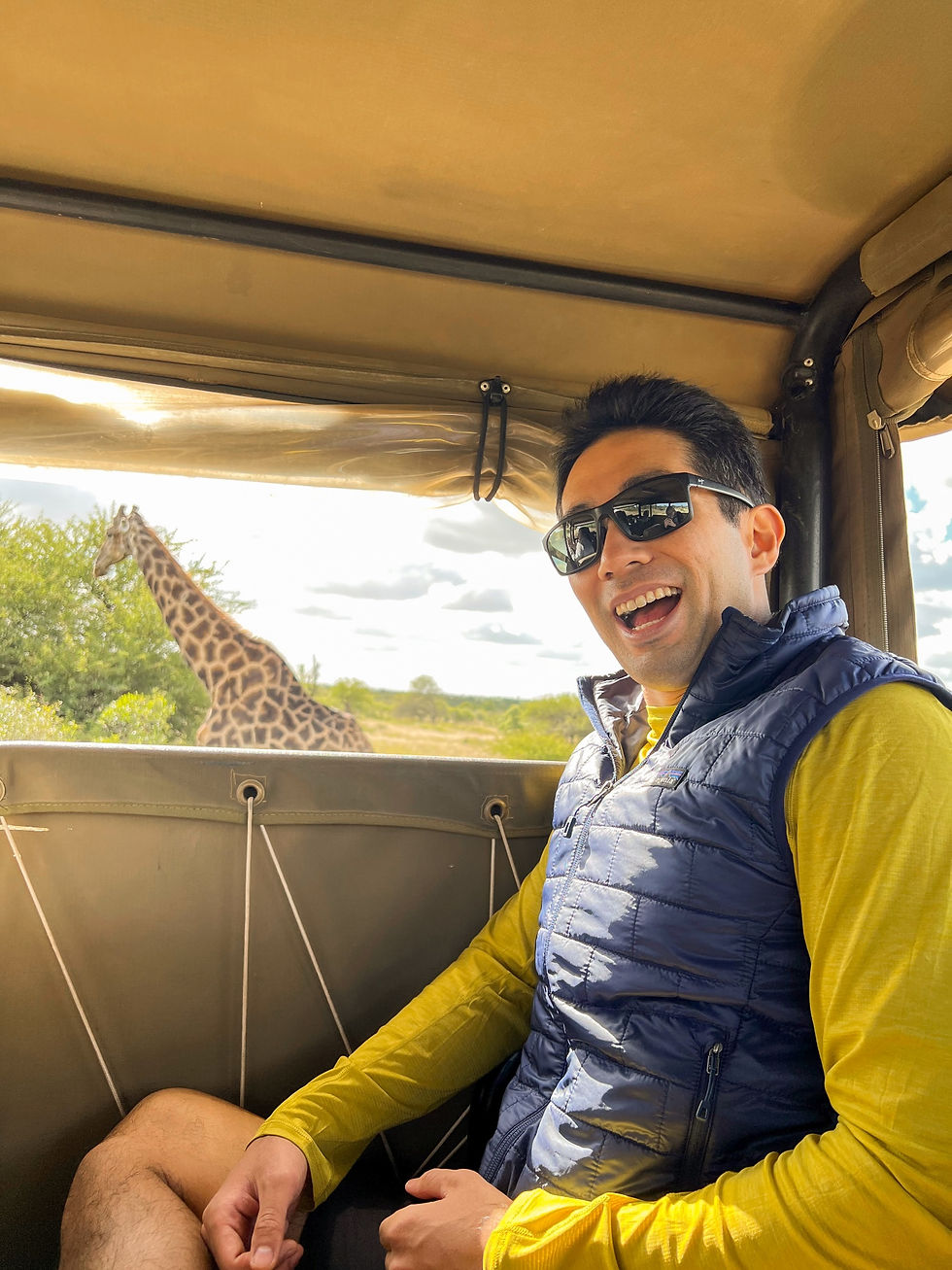 Solo traveler smiling in a jeep with a giraffe in the background on safari.