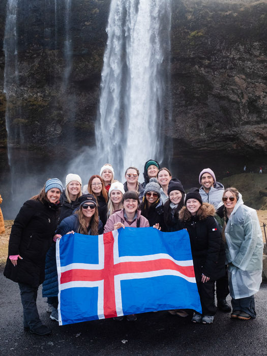 FTLO Travel group holding the Icelandic flag in front of a waterfall