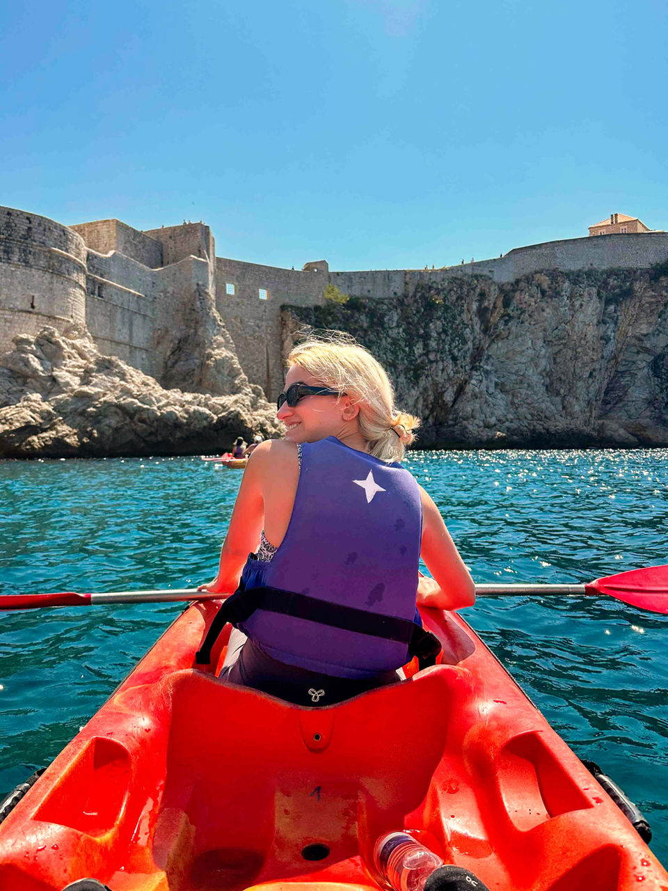solo traveler kayaking on the blue waters beneath Dubrovnik’s city walls