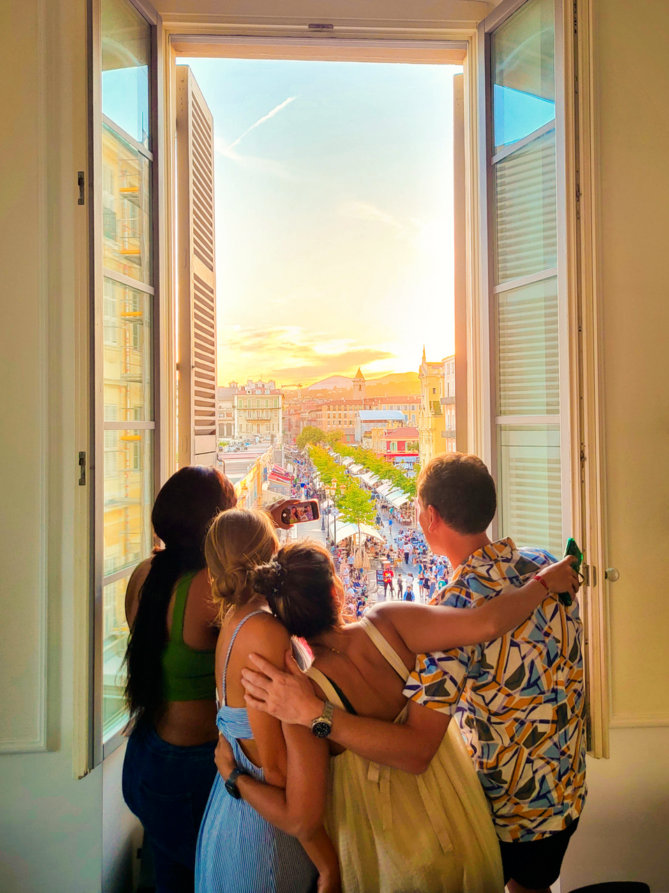Group of friends watching the sunset over Barcelona from a balcony window