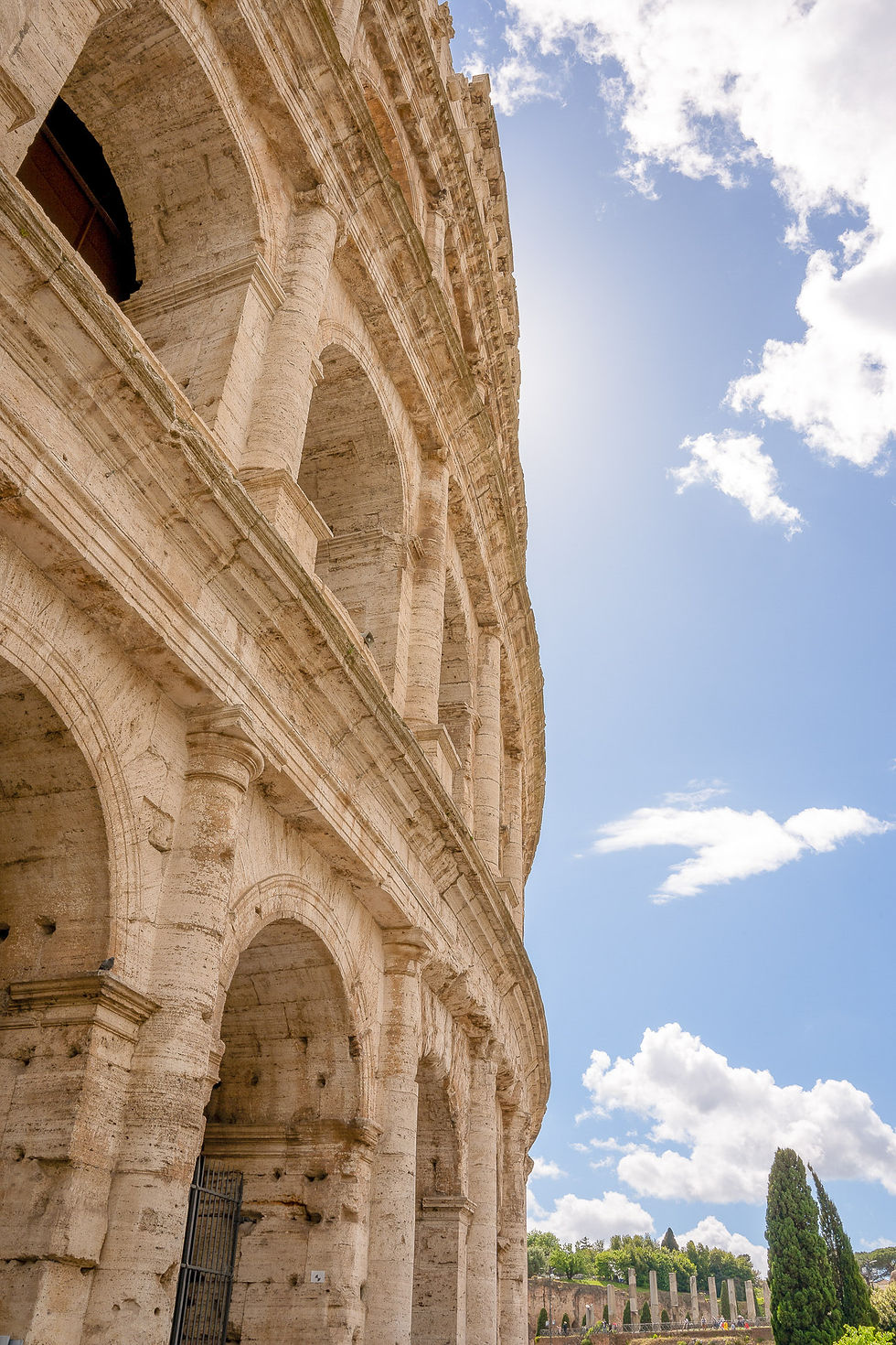 The Colosseum in Rome under a bright blue sky with clouds