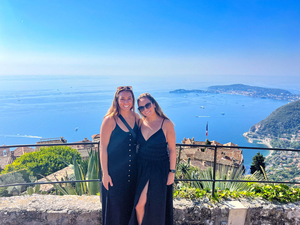 Two solo travelers posing with views of the French Riviera coastline