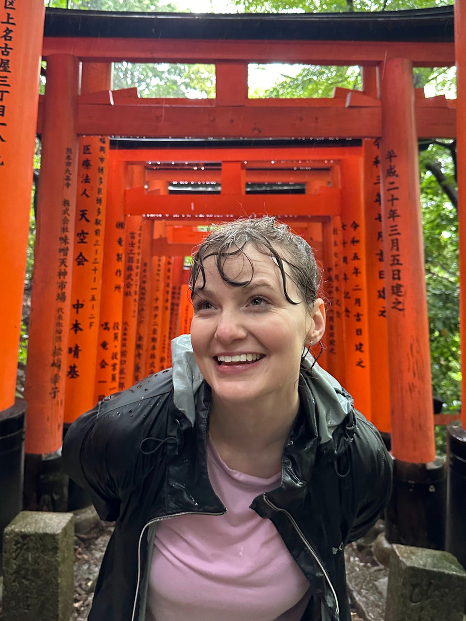 FTLO traveler smiling in the rain among the red Torii gates of Fushimi Inari.