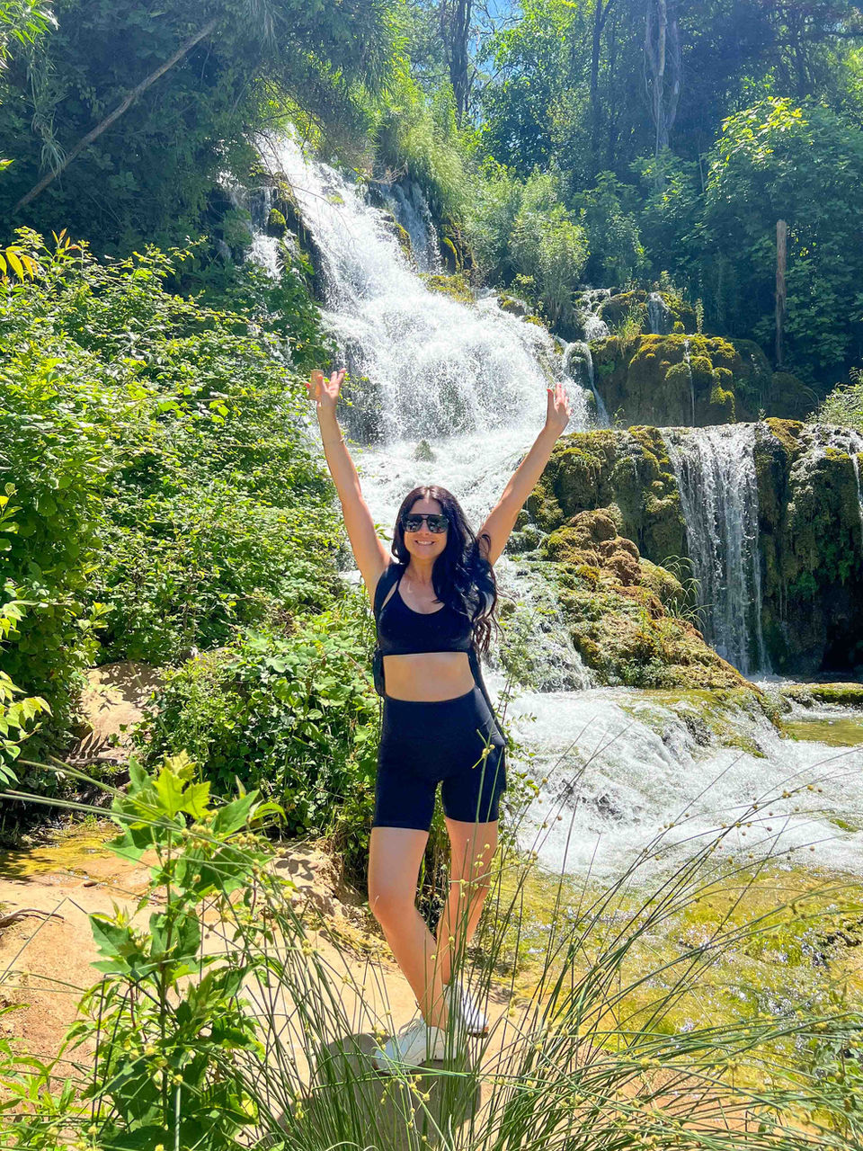 Traveler raising arms in front of a cascading waterfall at Krka National Park