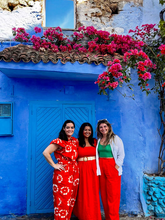 Three travelers posing by a blue-painted house with bougainvillea in Morocco