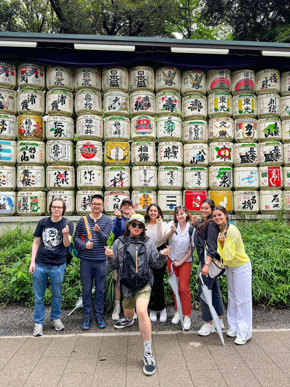 Group of FTLO travelers posing at Meiji Shrine with colorful sake barrels in Tokyo.