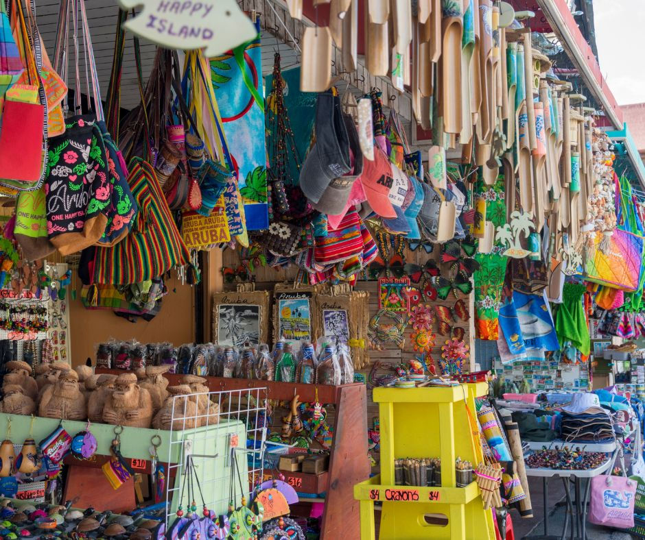 Vibrant souvenir shop with colorful bags, hats, and crafts. Signs read "Happy Island." Bright, tropical atmosphere with vivid patterns.