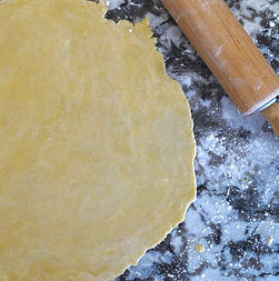 Rolled out pie dough on a floured countertop with a wooden rolling pin, showing homemade p