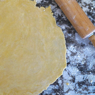 Rolled out pie dough on a floured countertop with a wooden rolling pin, showing homemade p