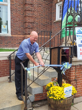 Gentleman cutting ribbon at the dedication ceremony for our Little Free Library at our Adult Learning Center.