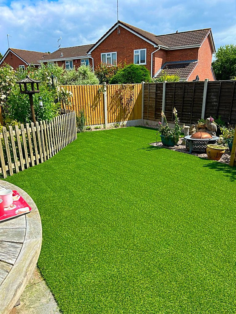Backyard with lush green artificial grass, wooden fence, and house.