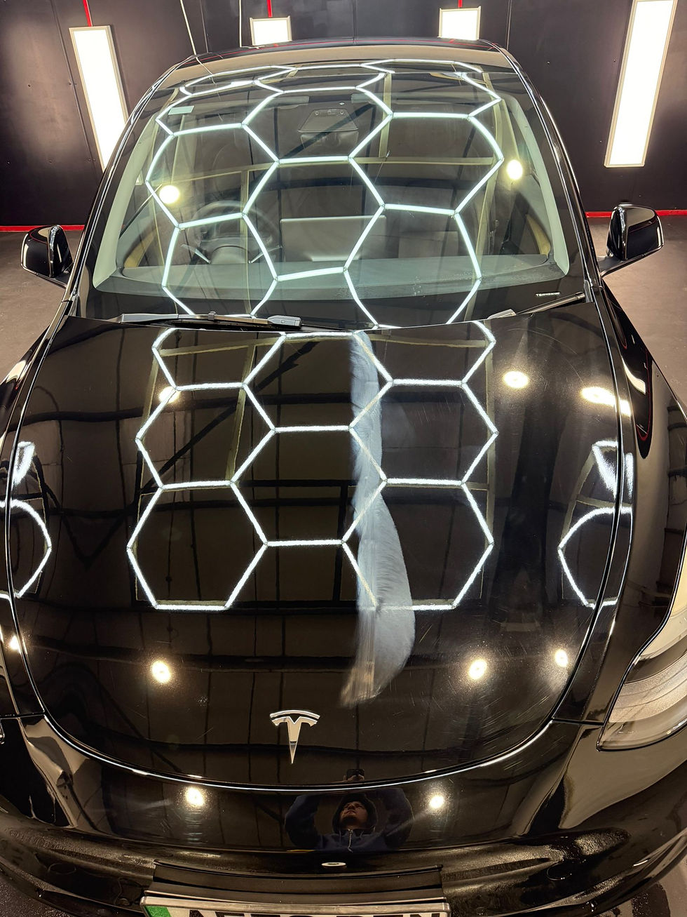 Black Tesla car reflecting hexagonal lights, showcasing Ceramic Coating Cheshire.